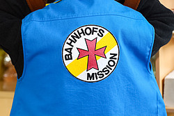 Das Logo der Bahnhofsmission auf einem Aufnäher auf einer Weste eines Helfers der Mission.