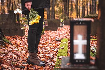 Person steht auf herbstlichem Friedhof