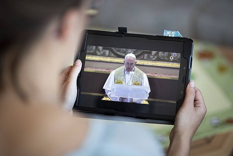 Frau betrachtet auf Tablet Gottesdienst mit Papst Franziskus
