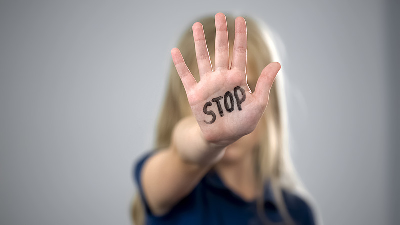 Mädchen mit ausgestreckter Hand vor dem Gesicht, auf der "Stop" steht.