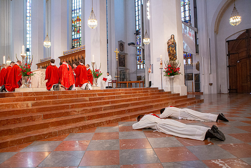 Zwei Männer liegen mit ausgestreckten Armen vor dem Altar auf dem Boden