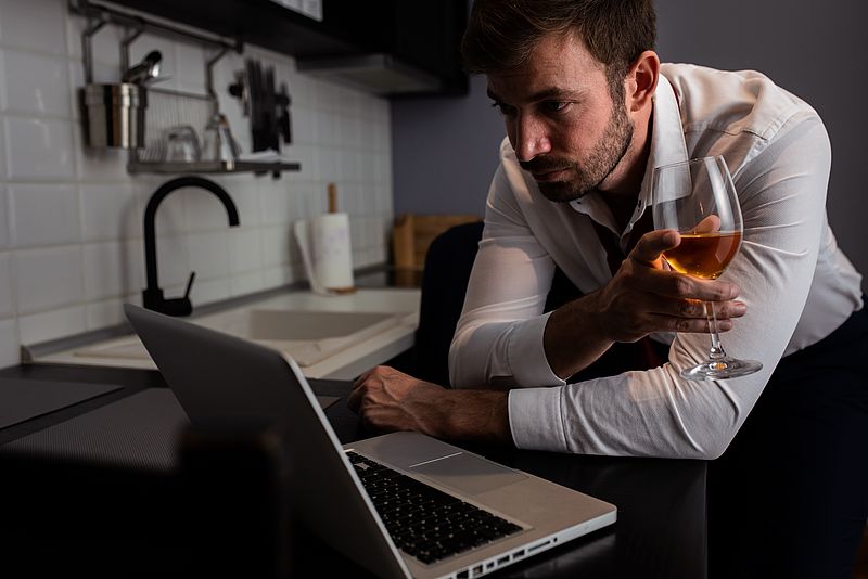 Mann mit Weinglas in der Hand steht vor Laptop