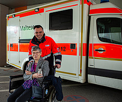 Michael Dzeba mit einer Dame im Rollstuhl vor einem Rettungsauto.