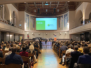 Blick in die Große Aula der LMU, in der Prof. Markus Vogt auf dem Podium eine Rede hält.