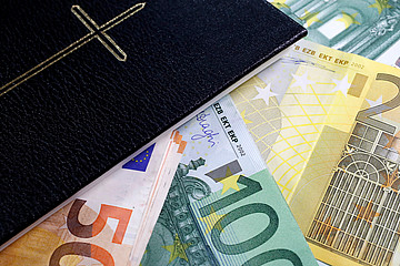 Ein Bündel Geldscheine liegt neben einer Bibel.