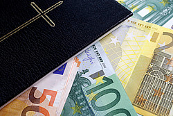 Ein Bündel Geldscheine liegt neben einer Bibel.