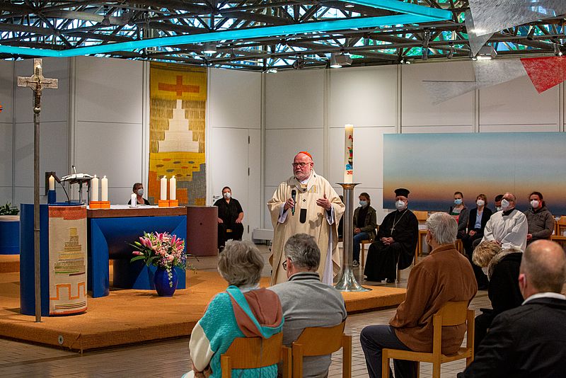 Kardinal Marx mit Mikrofon vor einem Altar um ihn herum sitzen Gottesdienstbesucher