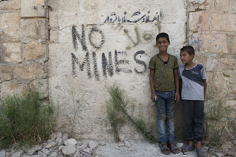 zwei syrische Kinder vor einer Mauer mit der Aufschrift "No mines".