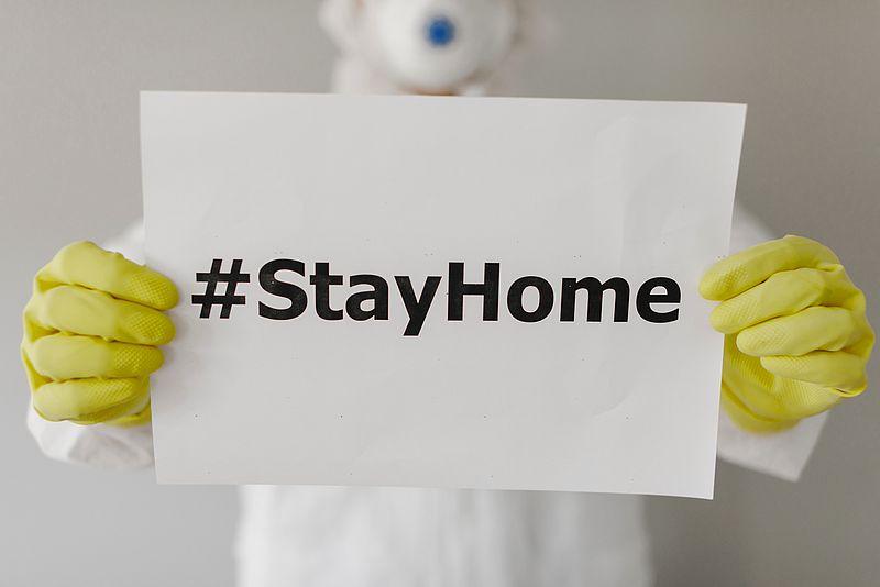 Mann in Schutzkleidung hält ein Schild auf dem "Stayhome" steht