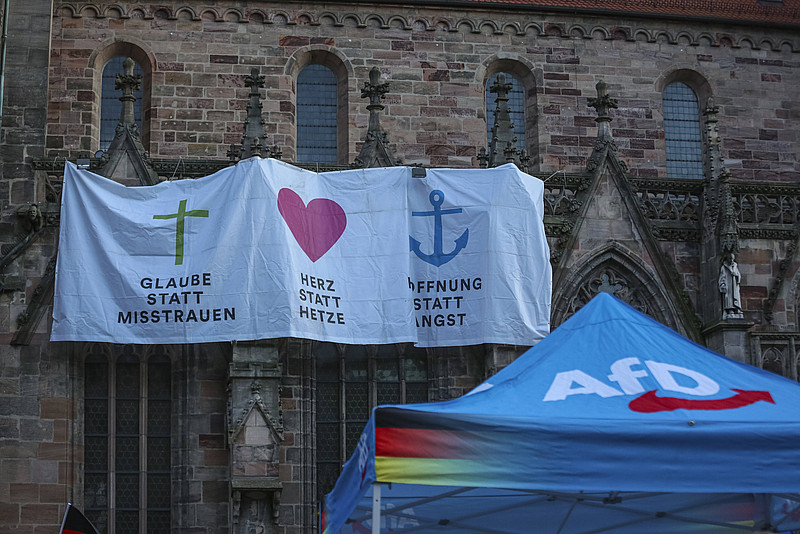 AFD-Wahlstand und Plakate an der Kirche. Dort steht "Glaube statt Hetze", "Herz statt Misstrauen" und "Hoffnung statt Angst"