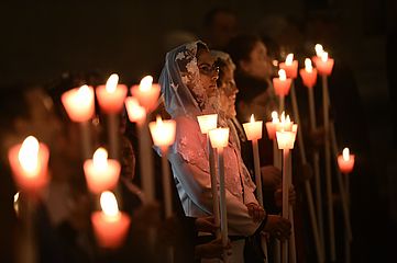 Menschen, darunter eine Frau mit Schleier, halten Kerzen an Mariä Lichtmess.