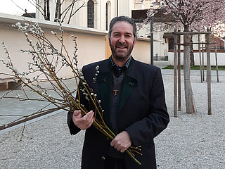Pfarrer Hans Speckbacher vor der Kirche mit Palmzweigen im Arm