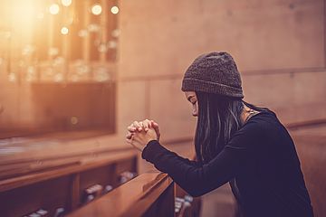 Frau sitzt betend mit gesenktem Blick in Kirchenbank