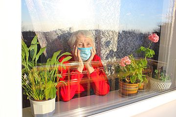 Seniorin mit Maske am Fenster