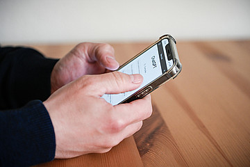 Ein Mann hält ein Smartphone in seinen Händen und betrachtet darauf den Chatbot 