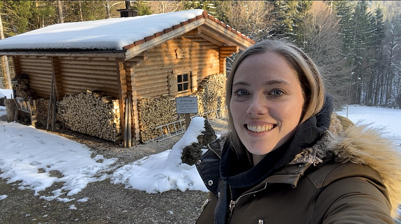 Zu sehen ist die Reporterin Anna Parschan vor einer Holzhütte mitten im Wald.