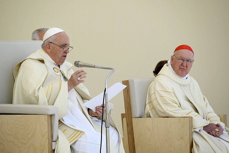 Papst Franziskus mit einem Papier in der Hand, soricht ins Mirko, im Hintergrund sitzt ein Mann