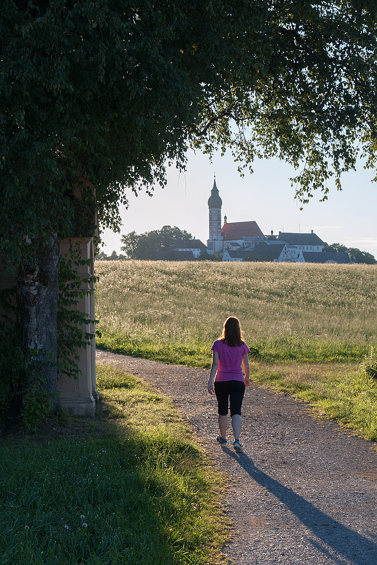 Frau läuft in der Abendsonne Richtung Kloster Andechs