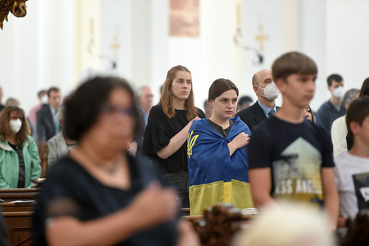 Menschen im Gottesdienst, eine junge Frau trägt eine Ukraine-Flagge um ihre Schultern