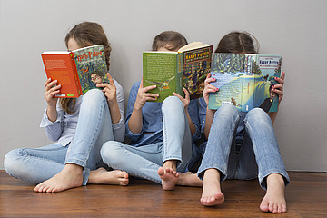 Drei Mädchen sitzen auf dem Boden vor einer weißen Wand und lesen Harry-Potter-Bücher.