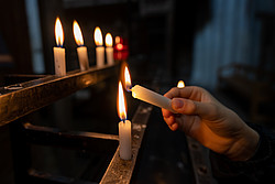 Hand hält Kerze, die an einer von vielen brennenden Kerzen angezündet wird.