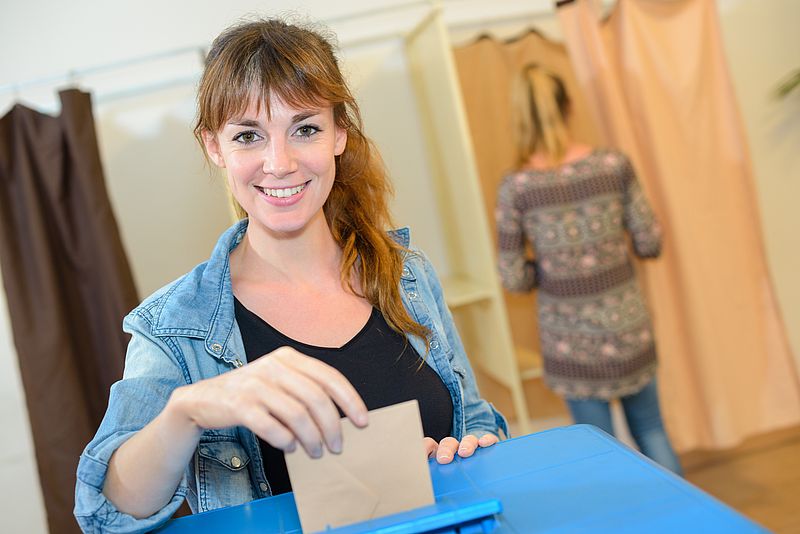Junge Frau beim Einwerfen von Wahlunterlagen in die Wahlurne