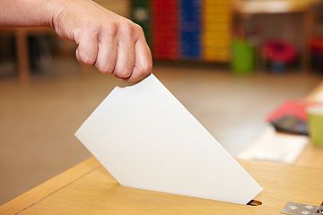 Stimmzettel wird in eine Wahlurne geworfen.