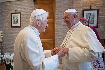 Der emeritierte Papst Benedikt XVI. und Papst Franziskus begrüßen einander herzlich.