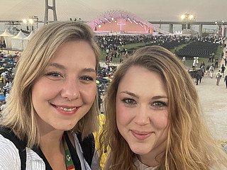 Zwei blonde Frauen lächeln in der Kamera und stehen vor einer Bühne.