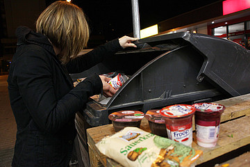 Frau holt Lebensmittel aus Müllcontainer