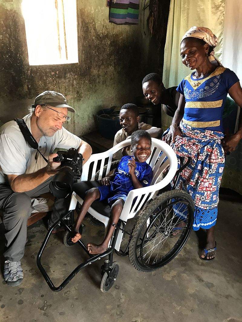 Fotograf kniet vor Kind im Rollstuhl