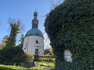 kleine Kapelle mit Kuppeldach und Türmchen im Grünen, umgeben von Efeu.