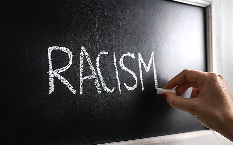 Hand schreibt das Wort "racism" an eine Tafel