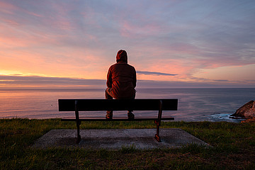 Mann sitzt auf einer Bank auf einer Klippe mit Blick aufs Meer