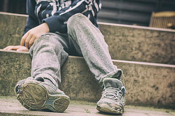 Kind sitzt auf Treppe mit schmutziger Hose und zerbeulten Schuhen