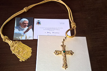 Kreuz auf einer Kiste, links daneben ein Biild von dem verstorbenen Papst em. Beneikt XVI. 
