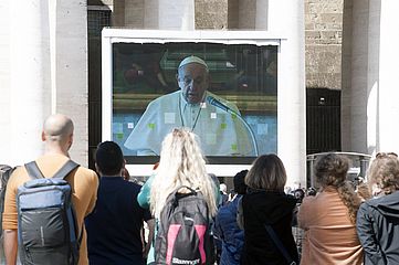 Menschen beobachten Übertragung der Papstmesse auf einer Leinwand