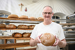 Mann in Backstube mit Brot in der Hand 
